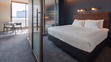 A hotel room with a large bed, a desk with a chair, a sliding glass door, and a city view.