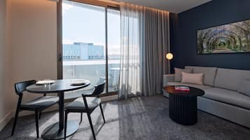A modern living room with a round dining table, two chairs, a sofa, a coffee table, and a large window with curtains.
