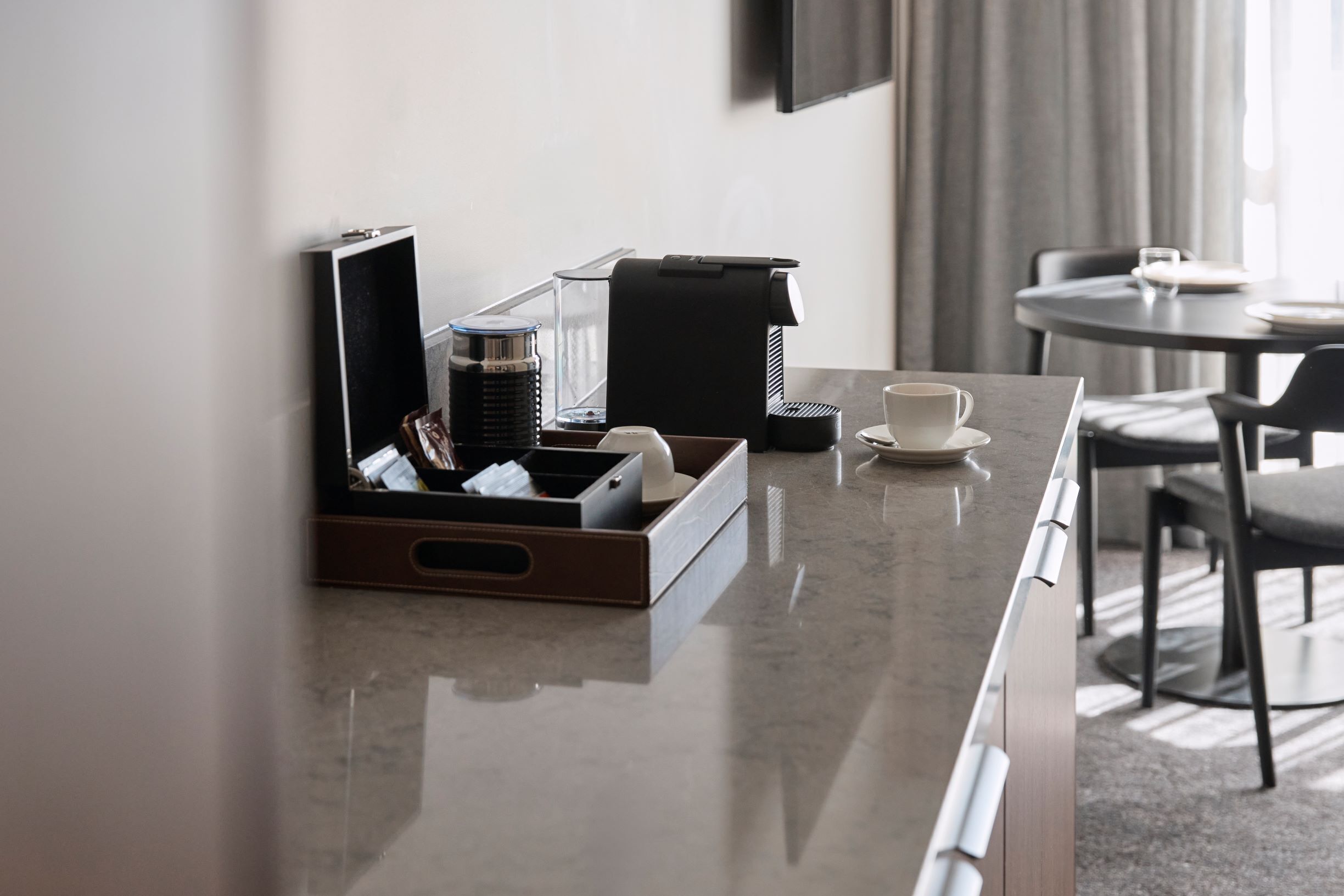 A hotel room with a marble countertop, a coffee maker, a cup, and a tray with various items.