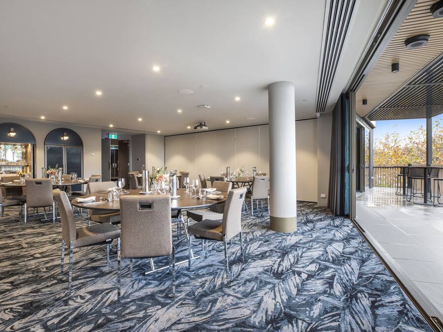 A spacious conference room with a large table and chairs, a patterned carpet, and a balcony with a view.