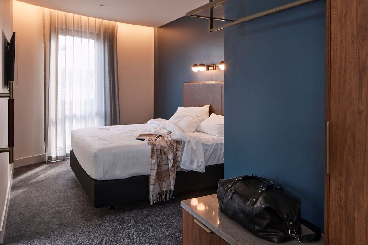 Et hotelværelse med en seng, et natbord, et fjernsyn og et vindue med gardiner.