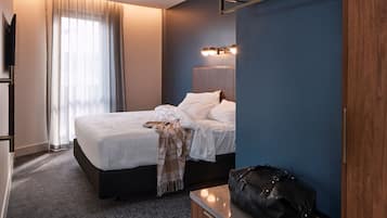 Una habitación de hotel con cama, mesita de noche, televisor y ventana con cortinas.