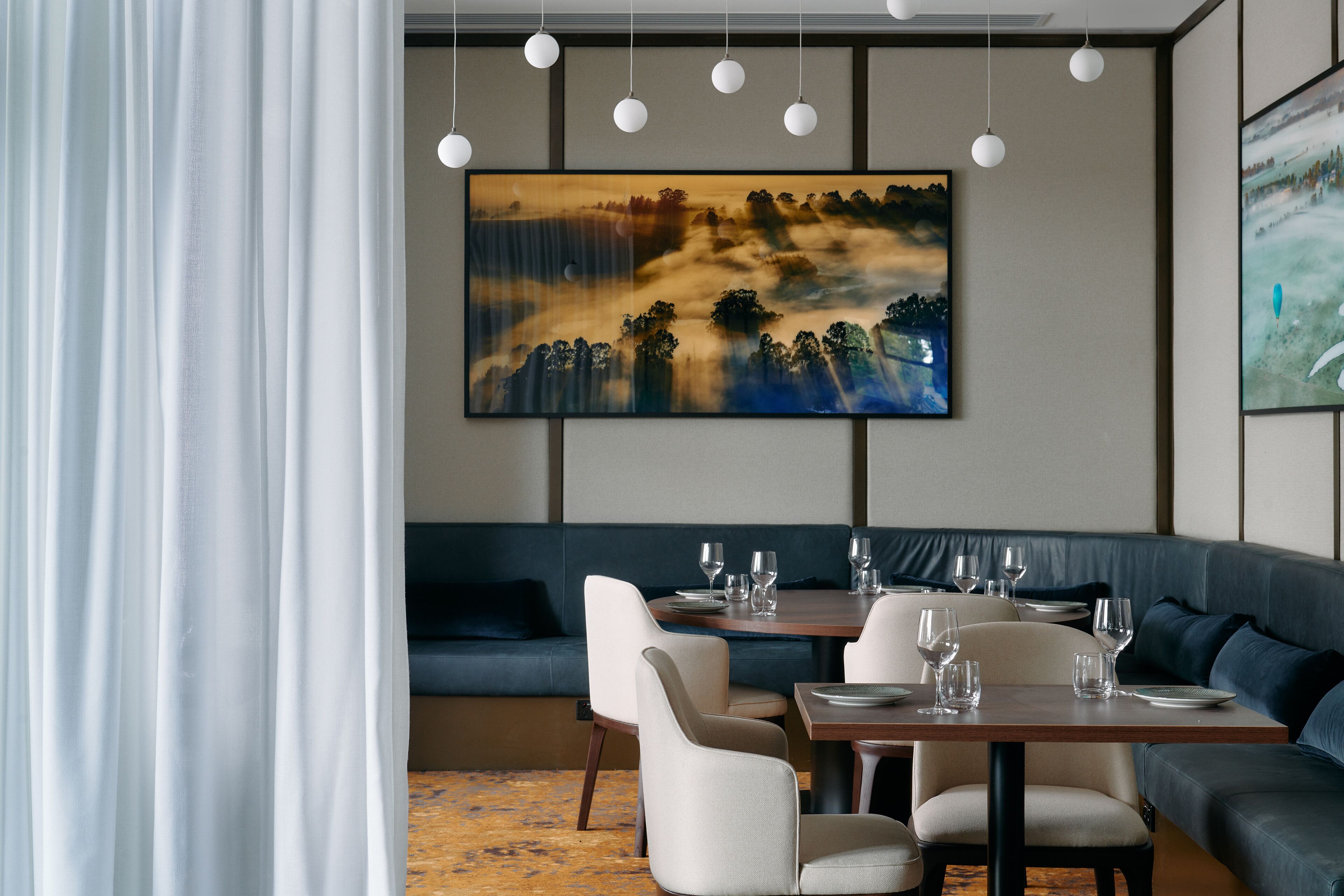Zona pranzo moderna con un grande quadro, un divano blu e un tavolo in legno apparecchiato per consumare un pasto.