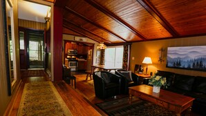 A cozy living room with a wooden ceiling, a fireplace, a dining area, and a kitchen in the background. - Special…rent 2 nights get the 3rd night…FREE! (Champion)