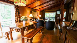 A rustic wooden dining area with a large table and benches, a stained glass light fixture, and a view of the outdoors. - Special…rent 2 nights get the 3rd night…FREE! (Champion)