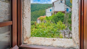 A rustic stone window frame with a view of a traditional white building with a red roof, surrounded by greenery and hills. - Vacation home Mickey by Interhome (Mošcenicka Draga)