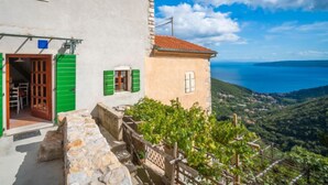 A two-story building with a stone staircase leading to a wooden door, a small balcony with a metal railing, and a view of a coastal landscape. - Vacation home Mickey by Interhome (Mošcenicka Draga)