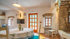 A dining area with a table set for two, a stone wall, and a kitchen in the background. - Vacation home Mickey by Interhome (Mošcenicka Draga)