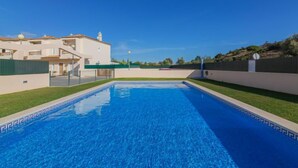 Une piscine à l’eau d’un bleu limpide, entourée d’un bâtiment blanc doté d’un toit en tuiles et d’une clôture verte.