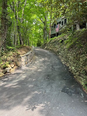 A paved road flanked by trees and a stone wall, leading to a building with an American flag.