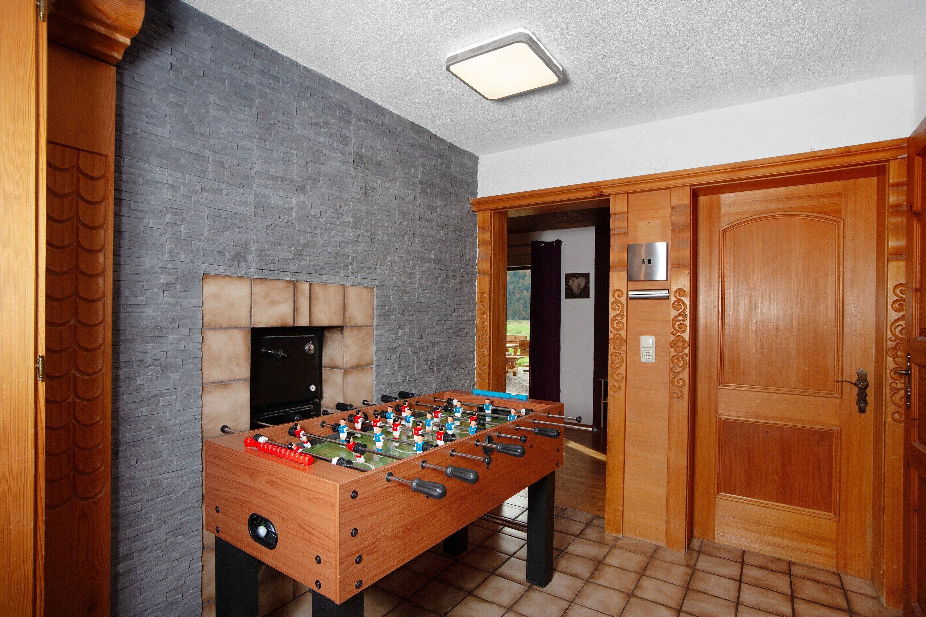 Una mesa de fútbolín en una habitación con pared de ladrillo, puerta de madera y suelo de baldosas.