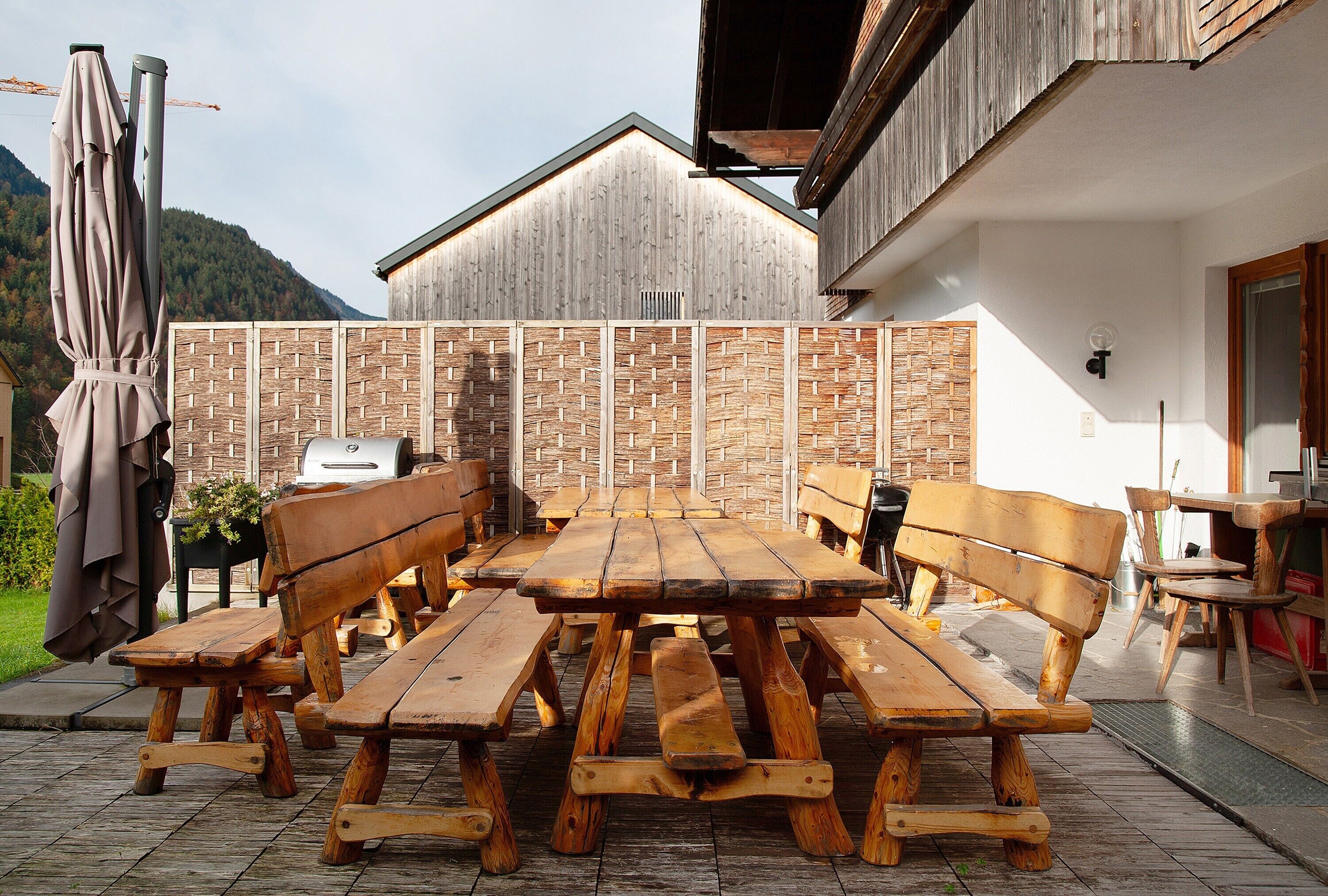 A wooden picnic table with benches, a barbecue grill, and a wooden fence in a backyard setting.