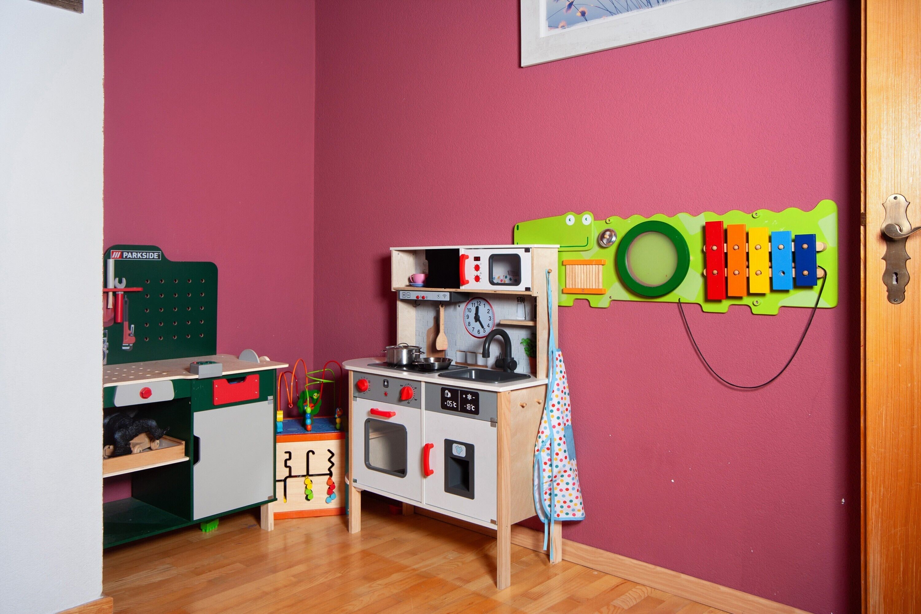 Ein Spielküchen-Set für Kinder vor einer roten Wand, mit einer Spielzeugeisenbahnstrecke und einer grünen Spielmatte in Froschform.