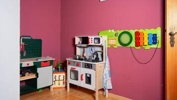 Ein Spielküchen-Set für Kinder vor einer roten Wand, mit einer Spielzeugeisenbahnstrecke und einer grünen Spielmatte in Froschform.