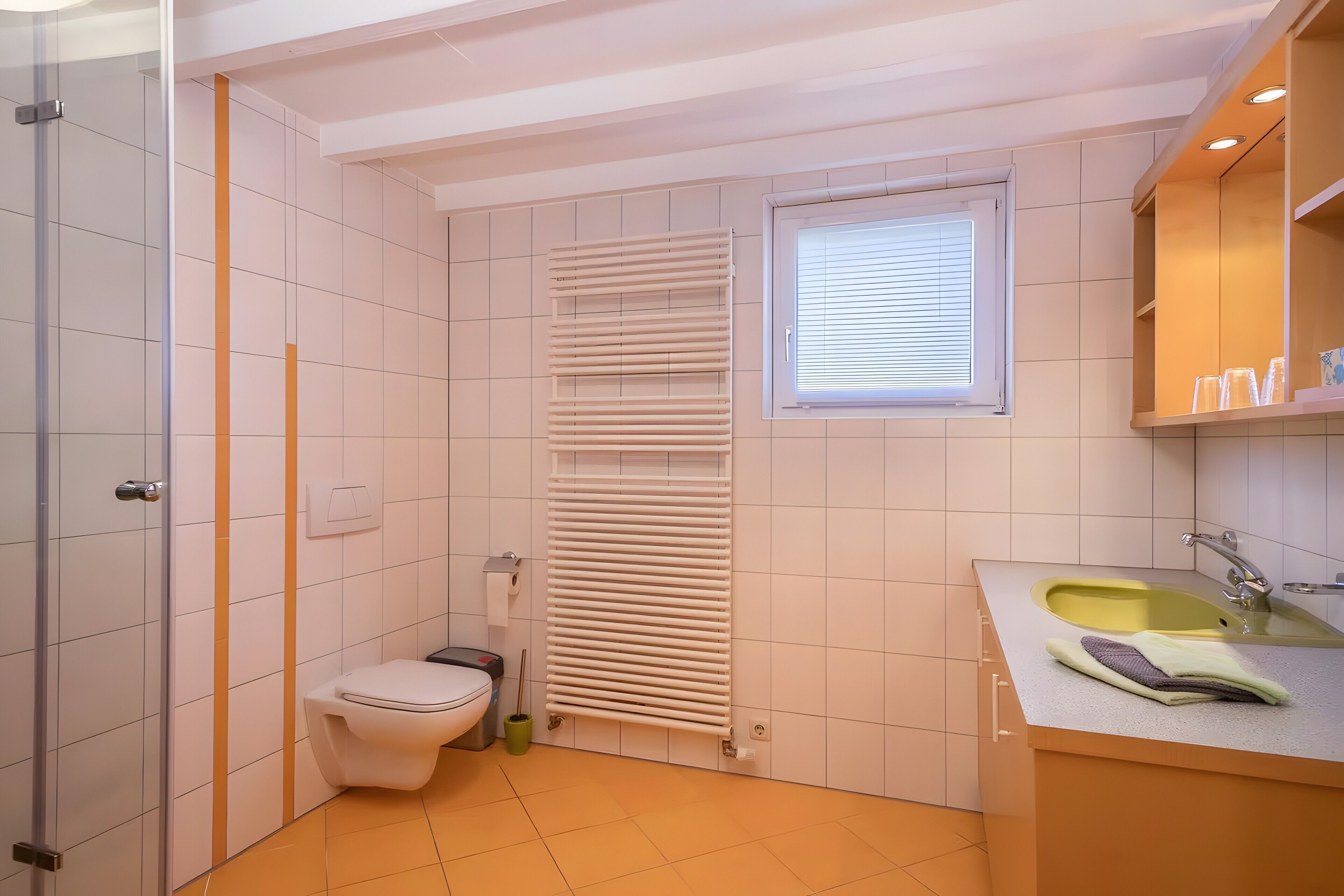 Ein kleines Badezimmer mit Toilette, Heizkörper, Fenster und Waschbecken inklusive Spiegel.