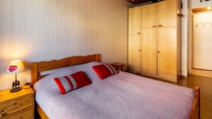 Une chambre avec un plafond en bois, un lit avec des oreillers rouges, une table de chevet avec une lampe et une armoire.