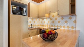 Une cuisine moderne avec des meubles en bois, un four à micro-ondes encastré et un panier de fruits posé sur le plan de travail.