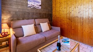 Une pièce chaleureuse avec un plafond en bois, un canapé marron agrémenté de coussins, une table en verre avec une bouteille et un verre, et un tableau encadré accroché au mur.