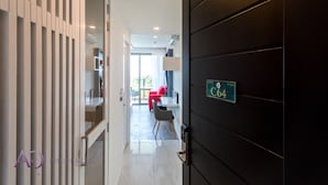 Ein moderner Hotelkorridor mit einer dunklen Tür mit der Aufschrift 'C64' und einem hellen Innenraum, der einen roten Sessel und einen Tisch zeigt.