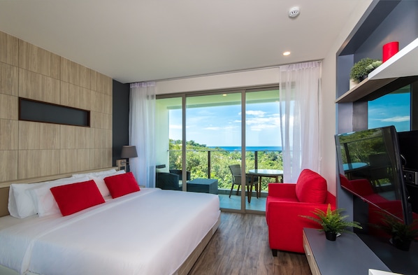 Une chambre d’hôtel moderne avec un grand lit, des touches de couleur rouge, un balcon avec une table et des chaises, et un téléviseur.