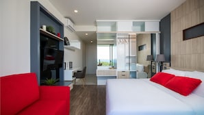 Ein modernes Hotelzimmer mit Bett, rotem Sofa, Fernseher, Schreibtisch und Blick ins Freie.