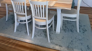 Een eetruimte met een houten tafel, witte stoelen, een blauwe kast en een decoratie van een surfplank aan de muur.