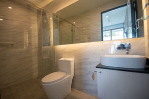 A modern bathroom with a glass-enclosed shower, a white toilet, and a sink with a mirror above.