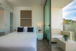 A modern hotel room with a bed, bedside table, lamp, and a balcony with a chair and potted plant.