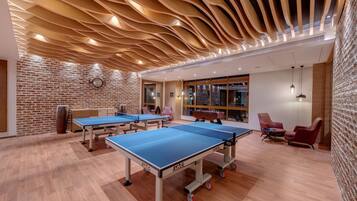 Una mesa de ping pong con superficie azul y ruedas, una pared de ladrillo y un techo de madera con diseño ondulado.