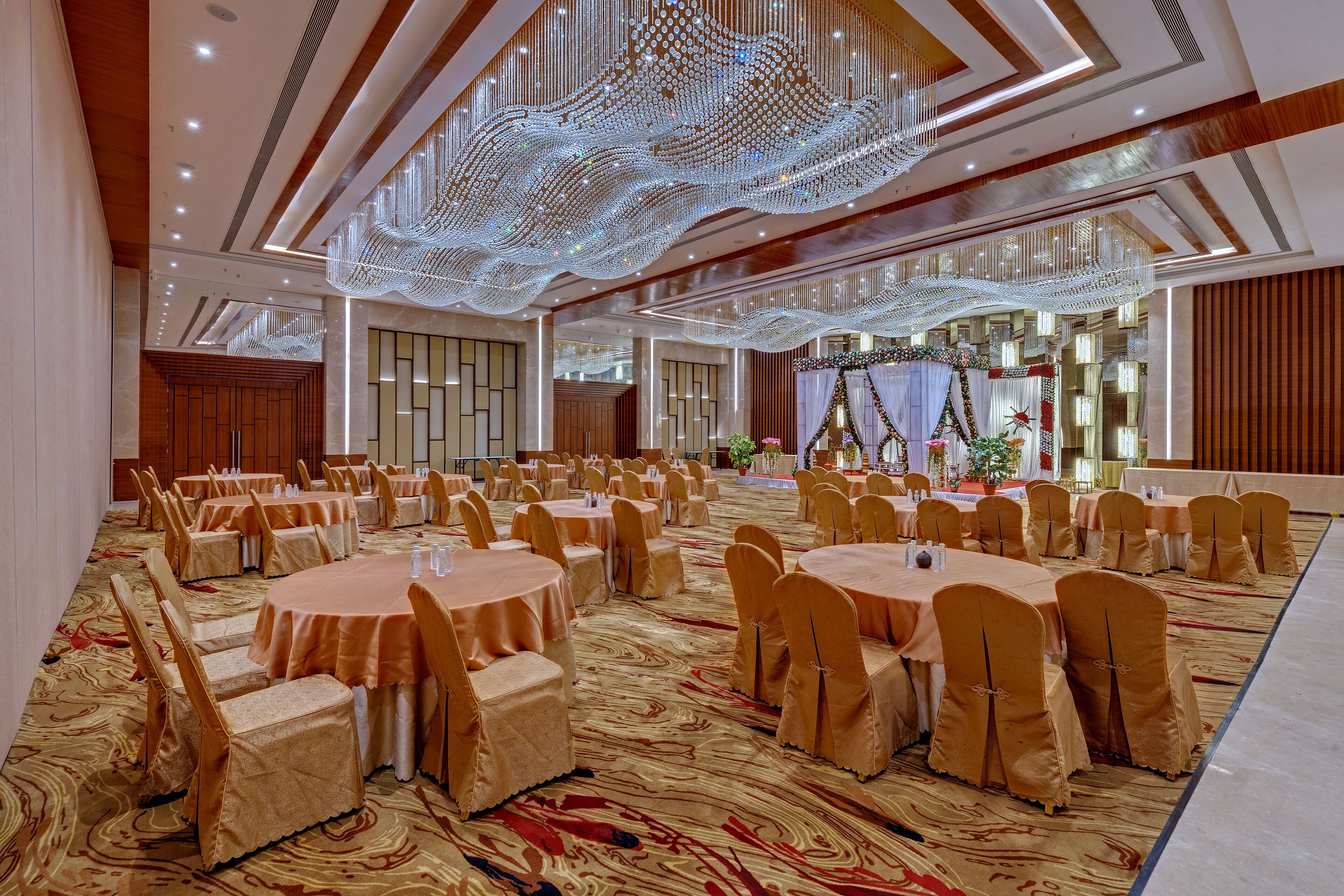 A banquet hall with round tables and chairs, a patterned carpet, and a decorative ceiling.