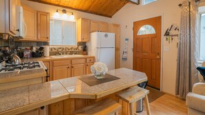 Una cocina con armarios de madera, un refrigerador, una estufa y un comedor con banco y mesa.