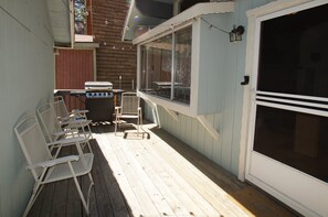 Un patio couvert avec un barbecue, des sièges d’extérieur et une porte-fenêtre coulissante.