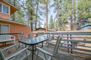 Une terrasse en bois, meublée de mobilier en métal, entourée de grands pins.