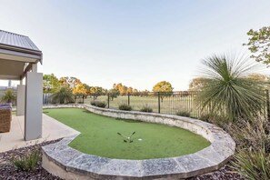 A backyard with a putting green, a stone border, and a house with a covered patio. - Back 9—Family-friendly Golf Lover’s Retreat (Dunsborough)