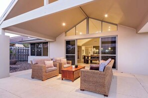 A modern outdoor living area with wicker furniture, a wooden coffee table, and a glass door leading to an interior space.