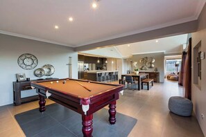 Amplia sala de estar con mesa de billar, cocina al fondo y comedor con decoración moderna.