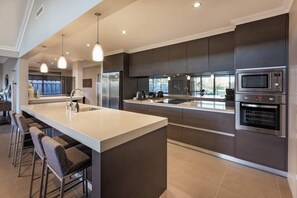 Una cocina moderna con una isla central, electrodomésticos de acero inoxidable, iluminación colgante y vistas al exterior.