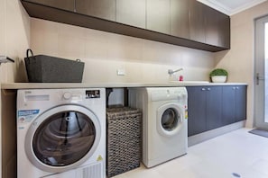 A compact laundry area with two washing machines, a sink, and a small potted plant. - Back 9—Family-friendly Golf Lover’s Retreat (Dunsborough)
