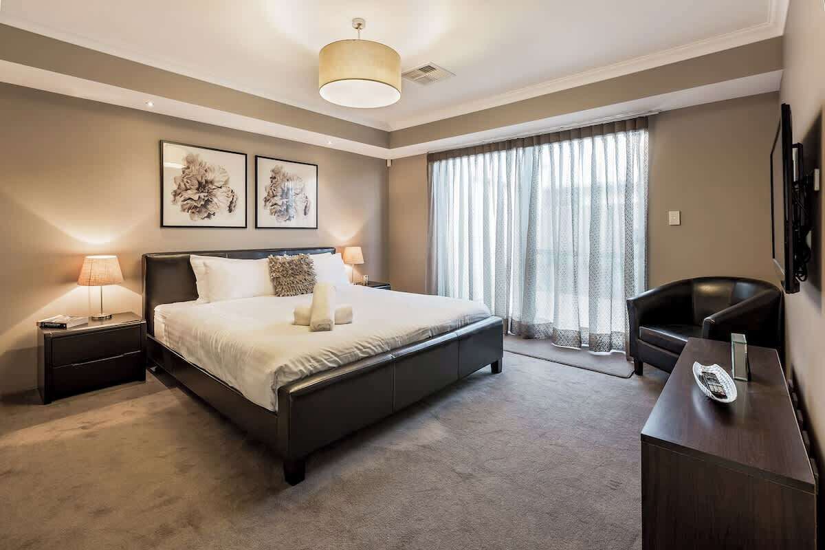 Un dormitorio moderno con una cama grande, lámparas de noche, un escritorio y una silla.