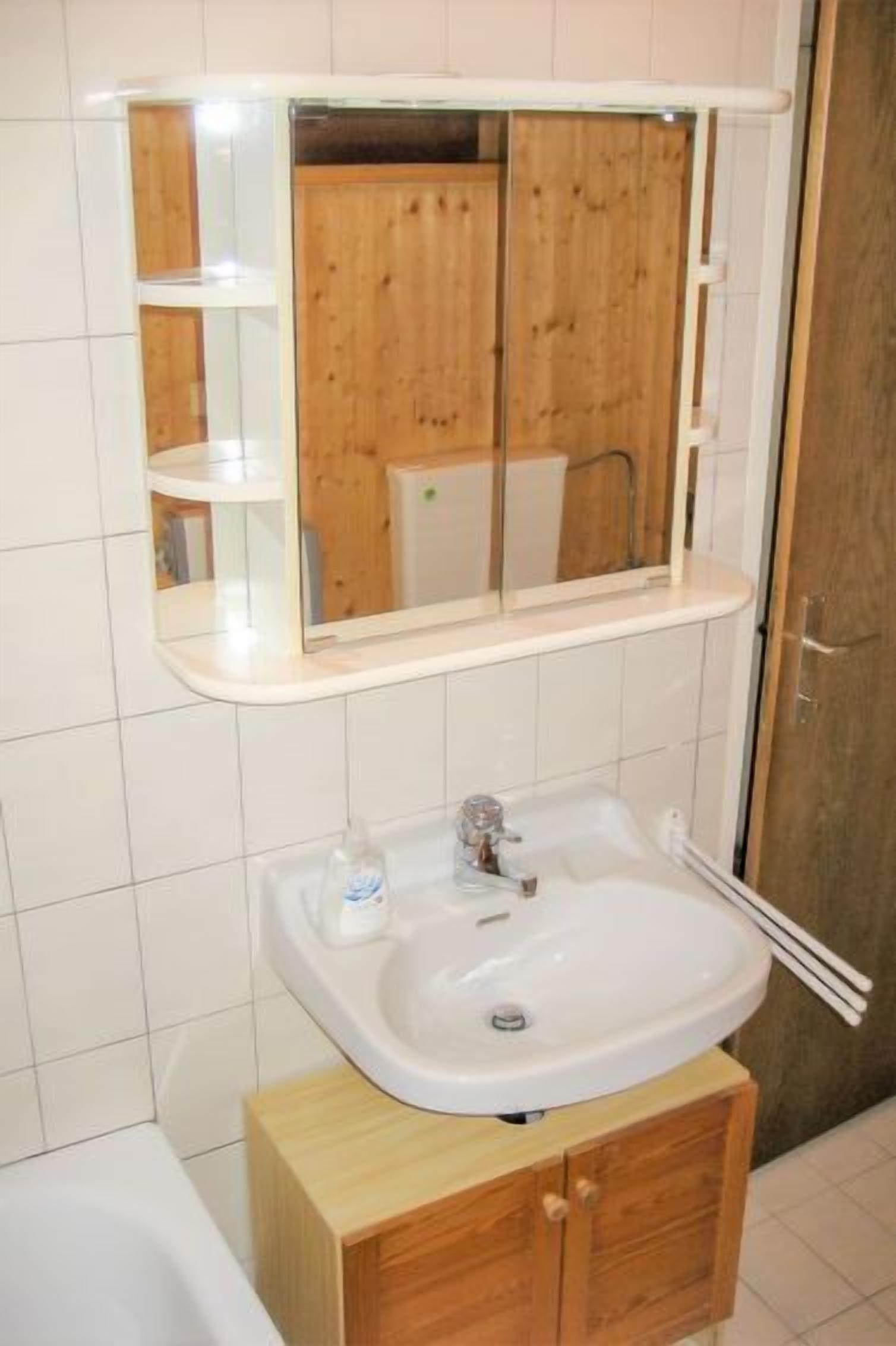 A bathroom with a white sink, wooden cabinet, and a mirror above the sink.