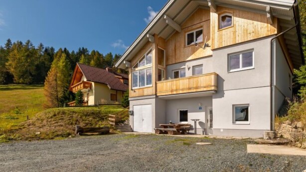 A two-story building with a wooden facade, a balcony, and a small attached structure with a table and chairs. - Pistenblick by Interhome (Sirnitz - Hochrindl)
