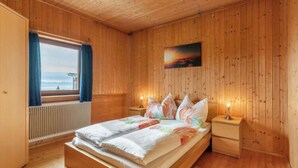 A wooden-paneled bedroom with a bed, a nightstand, a window with curtains, and a painting on the wall. - Pistenblick by Interhome (Sirnitz - Hochrindl)