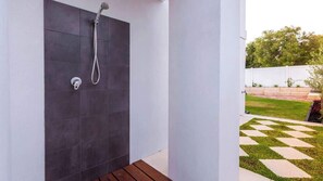 Un espace de douche extérieur moderne, avec des carreaux sombres, un banc en bois et une pelouse à motifs à carreaux.