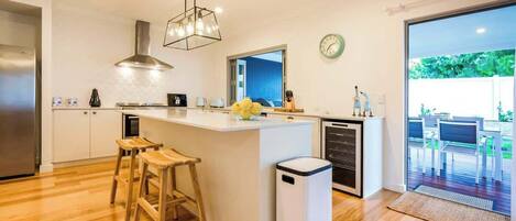 Een moderne keuken met een centraal eiland, houten krukken, een rvs-afzuigkap en een groot raam met uitzicht op een terras.