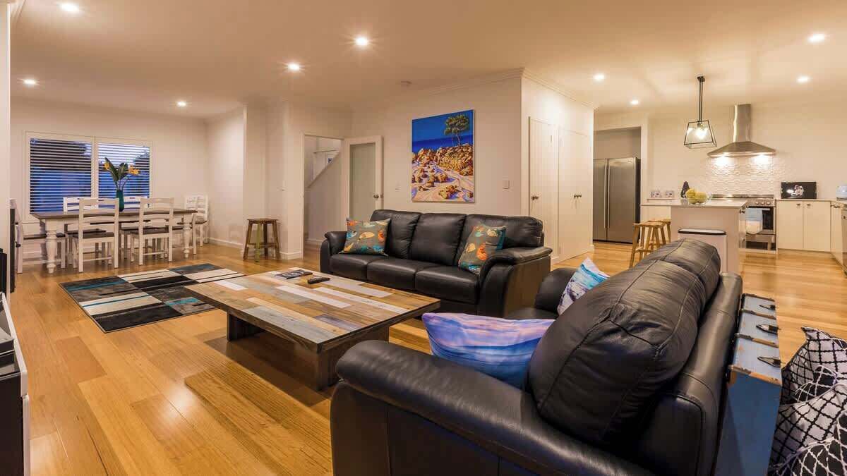 A modern living room with a black leather sofa, a coffee table, and a dining area with white chairs.
