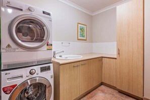 A laundry room with a front-loading washer and dryer, a sink, and wooden cabinets.