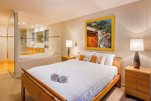Une chambre d’hôtel avec un grand lit, une salle de bain avec une baignoire, un miroir et un tableau au mur.