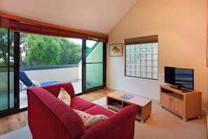 Un salon avec un canapé rouge, un téléviseur posé sur un meuble en bois et une porte-fenêtre coulissante donnant sur un espace extérieur.