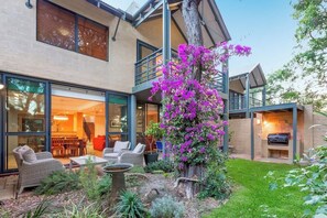 Une maison moderne dotée d’un patio, de mobilier d’extérieur et d’un grand arbre en fleurs.