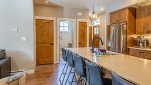 A modern kitchen with a large island, bar stools, a built-in espresso machine, and wooden cabinetry.